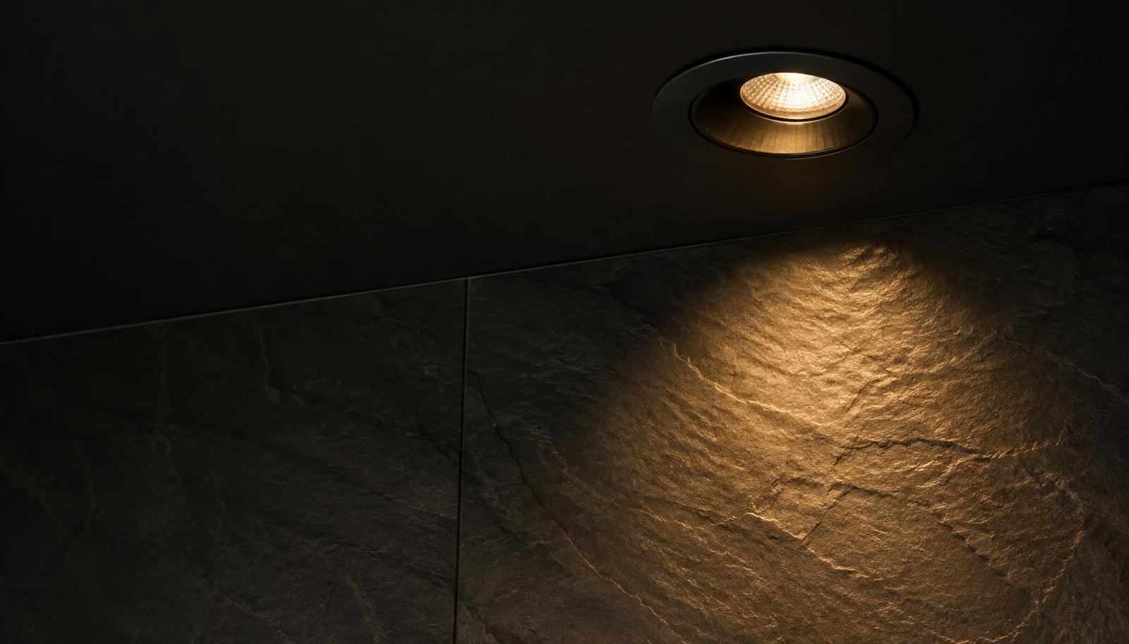 Recessed COB downlight casting a controlled warm beam across a textured stone wall